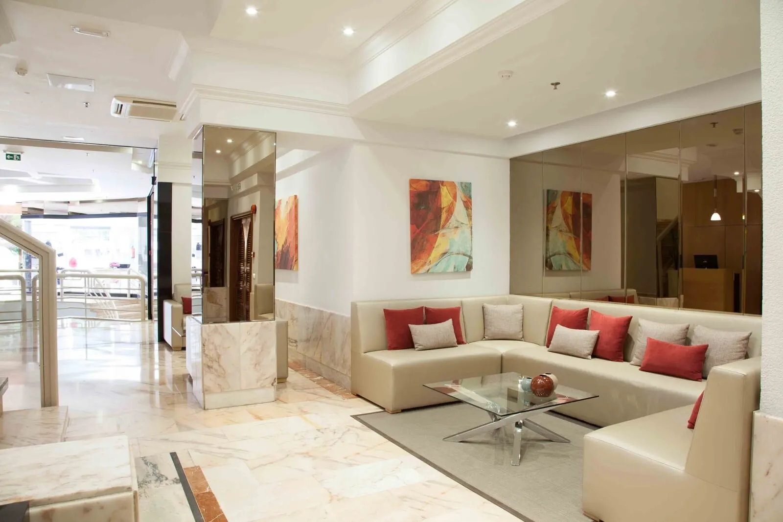Hotel Príncipe Paz: A modern lobby with a marble floor, a beige sectional sofa with red and white cushions