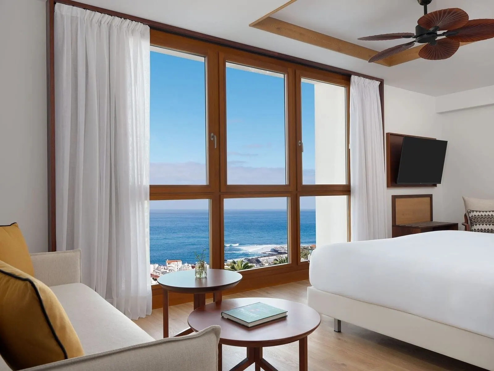 Gran Hotel Taoro: A hotel room with a large window, a bed, a sofa, a small table, and a ceiling fan