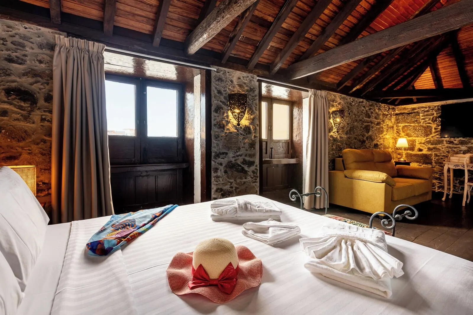 Hotel Duque de la Torre: A room with a bed, a chair, a stone wall, and a wooden ceiling