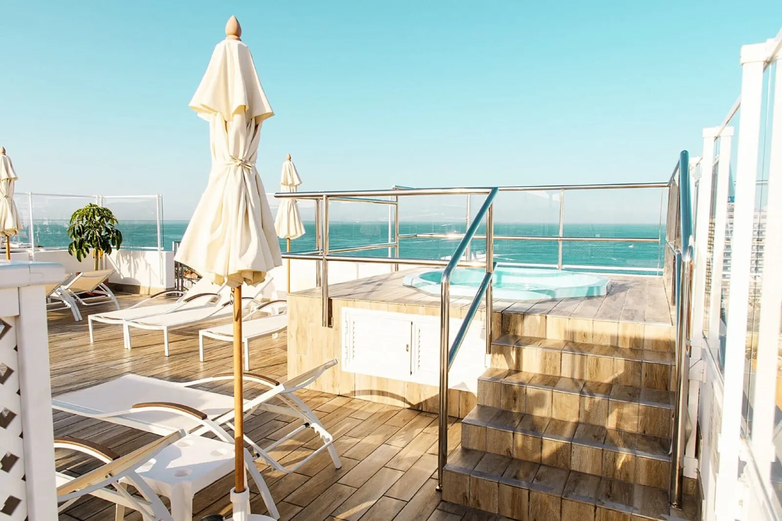 Coral Ocean View: A sunlit outdoor deck with lounge chairs, a hot tub, and a clear view of the ocean