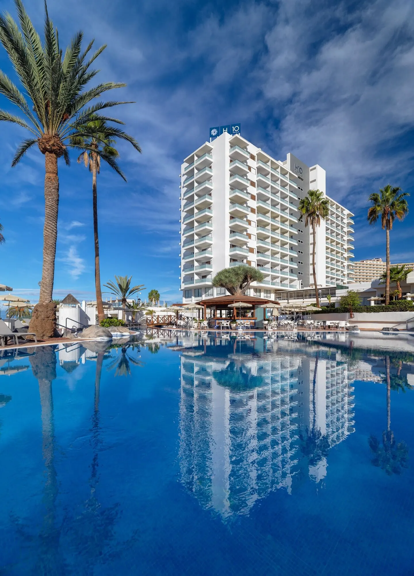 H10 Gran Tinerfe: A hotel with a pool, palm trees, and a clear blue sky