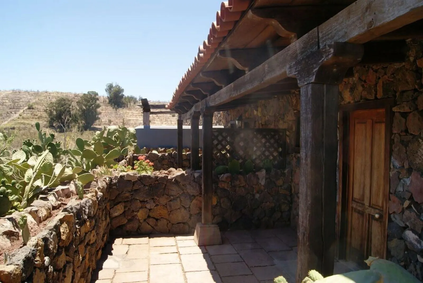 Hotel Rural Caserío Los Partidos: A stone-walled patio with a wooden door, a stone wall with cacti