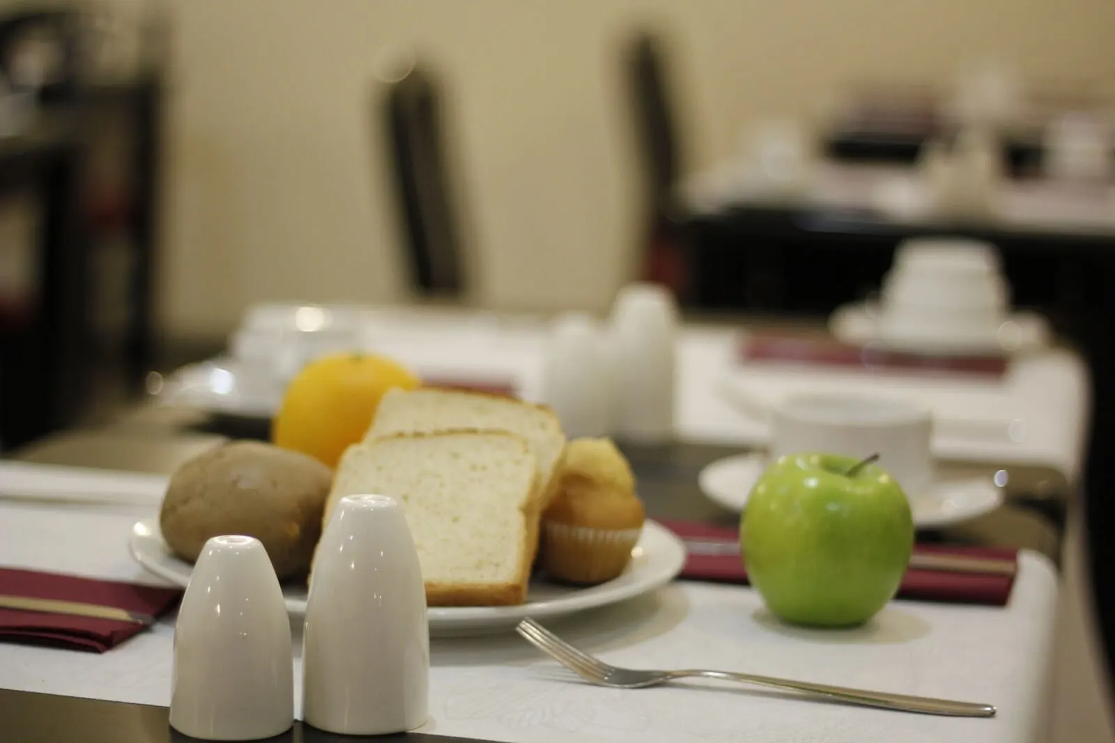 4Dreams Hotel: A breakfast table with bread, a muffin, a green apple, and salt and pepper shakers