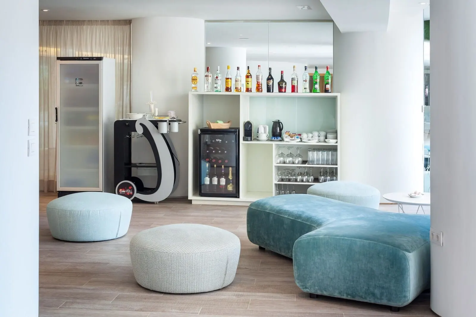 Tigotan Lovers & Friends: A modern living room with a kitchen area, including a refrigerator, a coffee machine