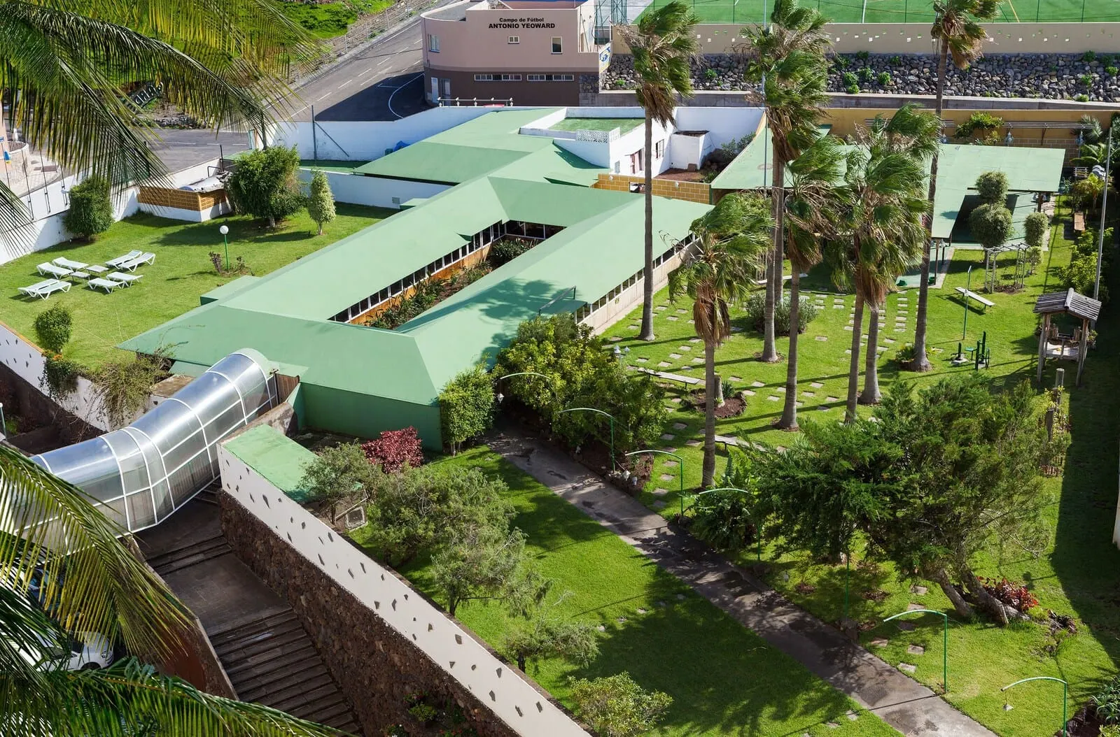 Hotel Panorámica Garden: A hotel with a green roof, palm trees, and a covered walkway