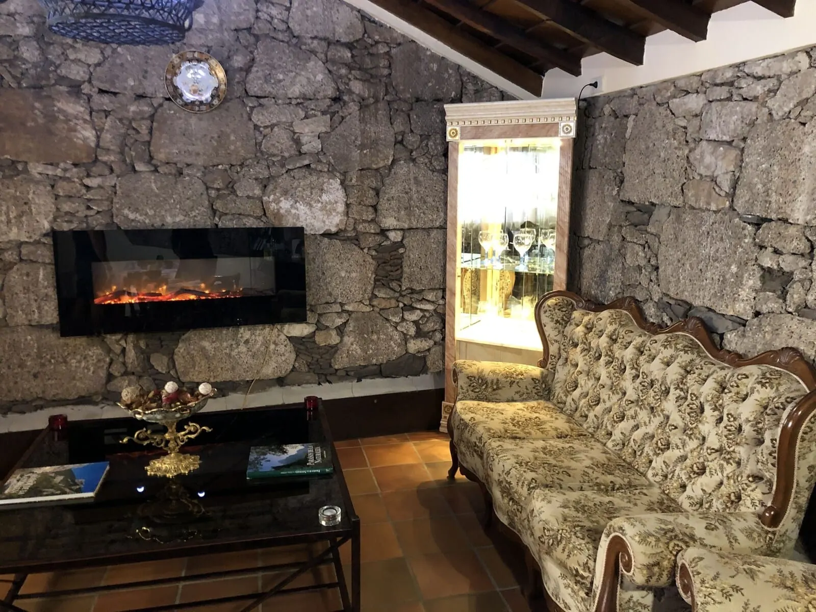 Hotel Rural Vilaflor: A room with a stone wall, a fireplace, a sofa, and a table with a vase and book