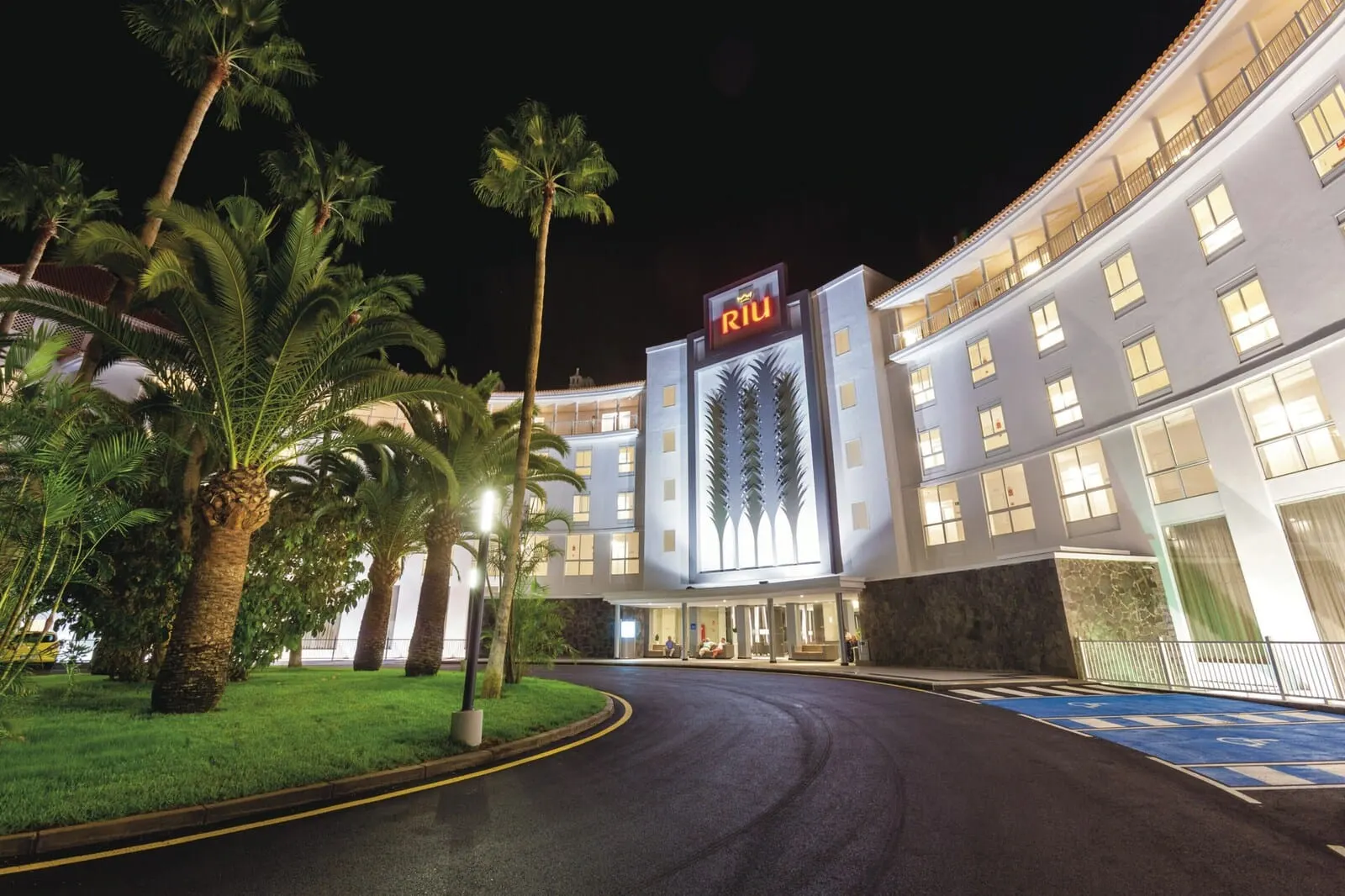 Hotel Riu Arecas: A hotel with a modern facade, palm trees, and a well-lit entrance
