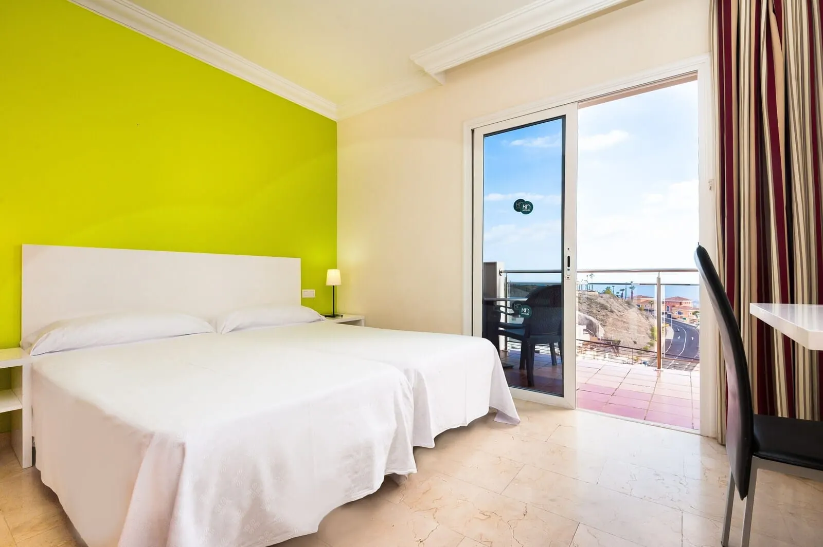 KN Aparthotel Panorámica: A hotel room with a large bed, a bright green wall, a balcony with a view, and a chair