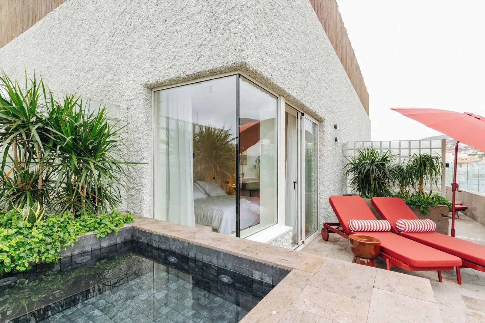 Hotel Taro Santa Cruz: A modern hotel room with a glass door, a small pool, and red lounge chairs