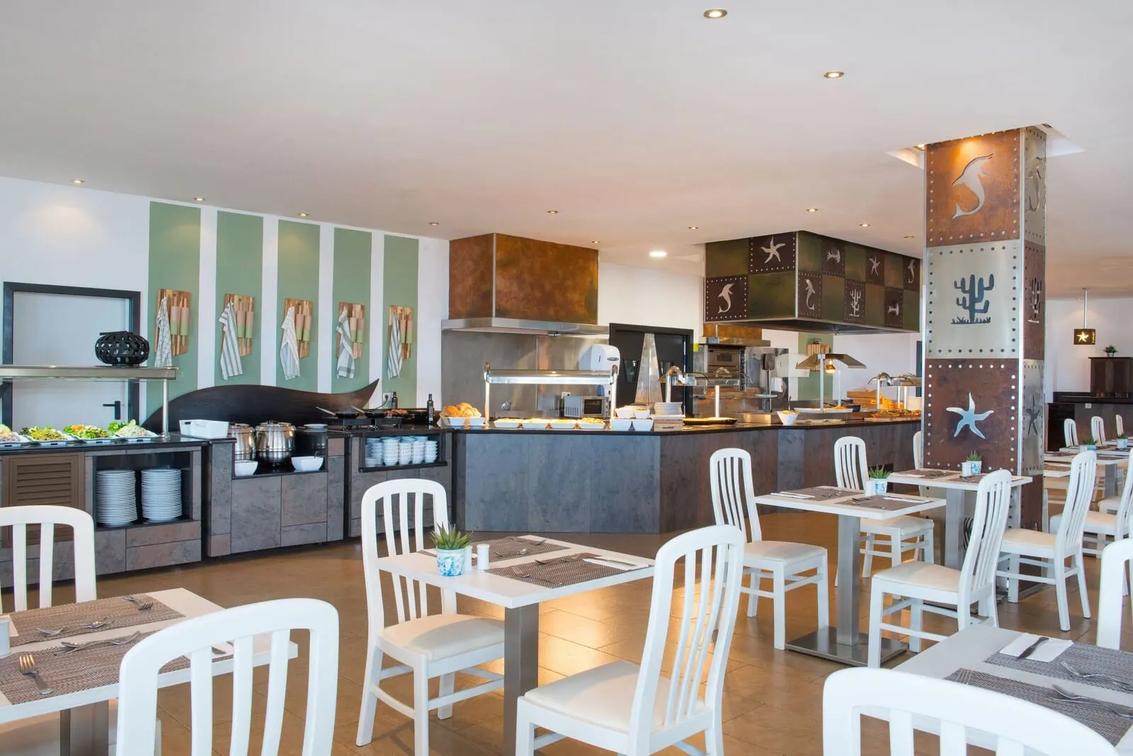 Iberostar Waves Bouganville Playa: A modern restaurant with a central bar, white chairs, and a buffet area