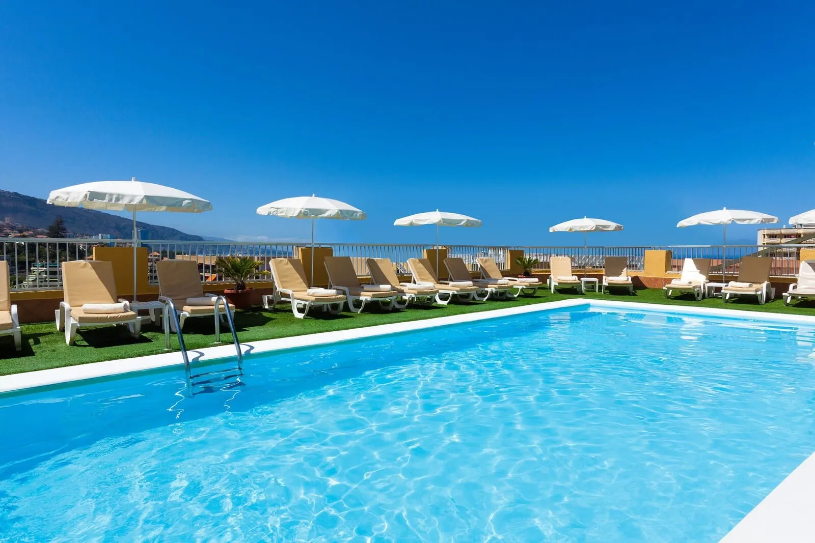 GF Noelia: A pool area with lounge chairs and umbrellas, a clear blue sky