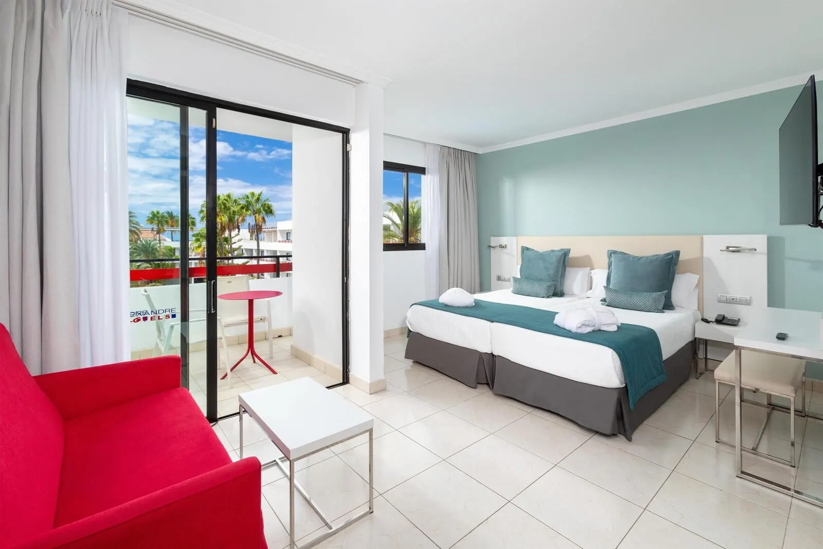 Alexandre La Siesta: A hotel room with a bed, a desk, a chair, and a balcony with a view of palm trees