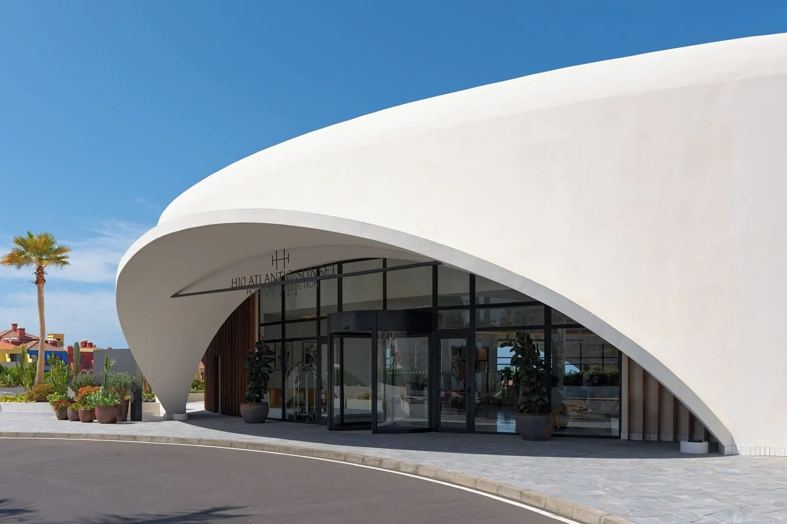H10 Atlantic Sunset: A modern building with a curved white facade, large glass entrance, and a clear sky