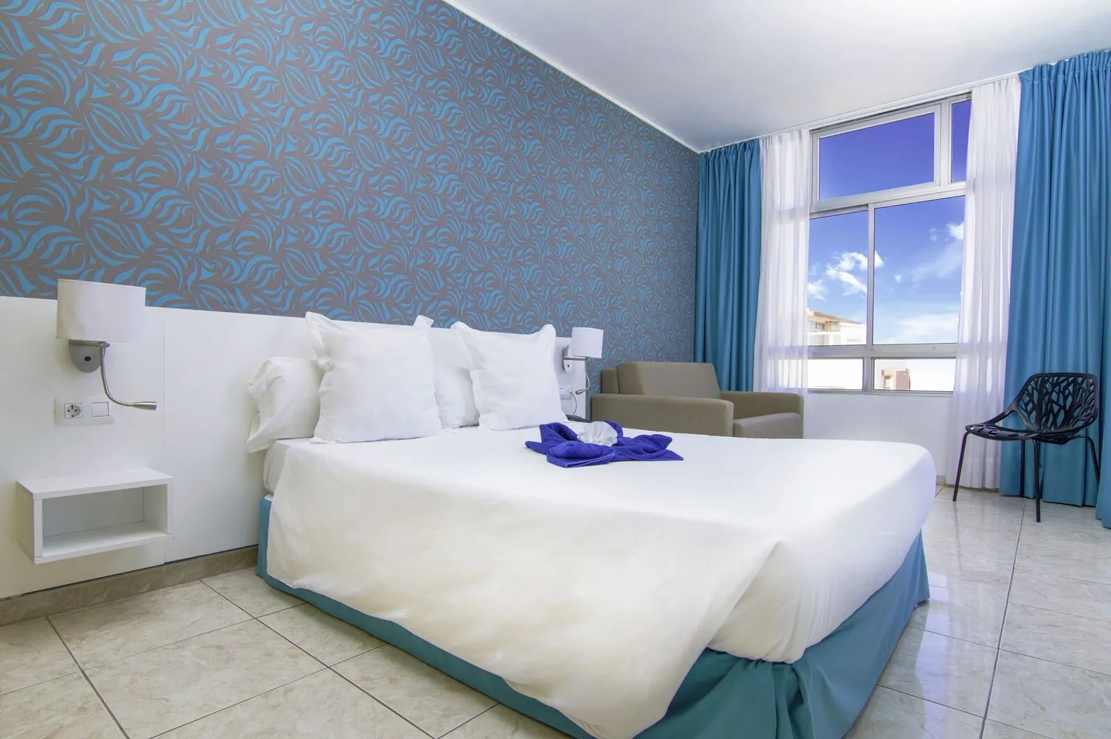 Checkin Concordia Playa: A hotel room with a large bed, a chair, a desk, and a window with curtains