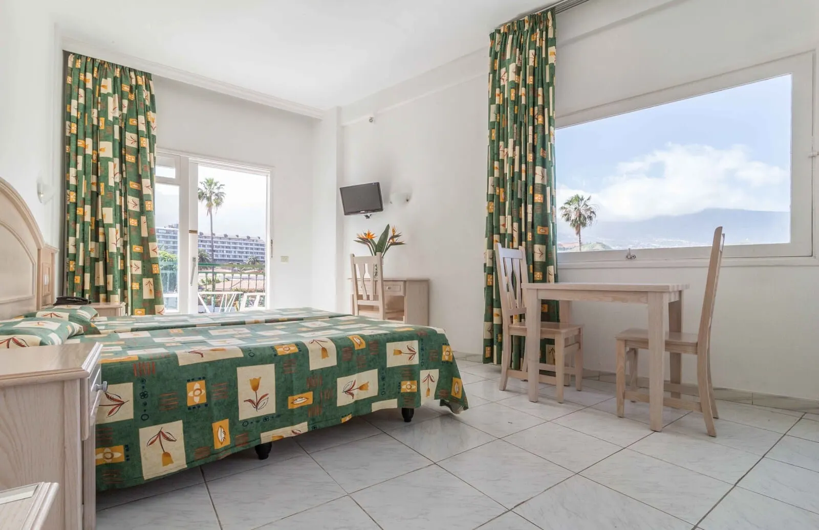 Apartamentos La Carabela: A hotel room with a bed, a desk, a chair, a TV, and a balcony with a view