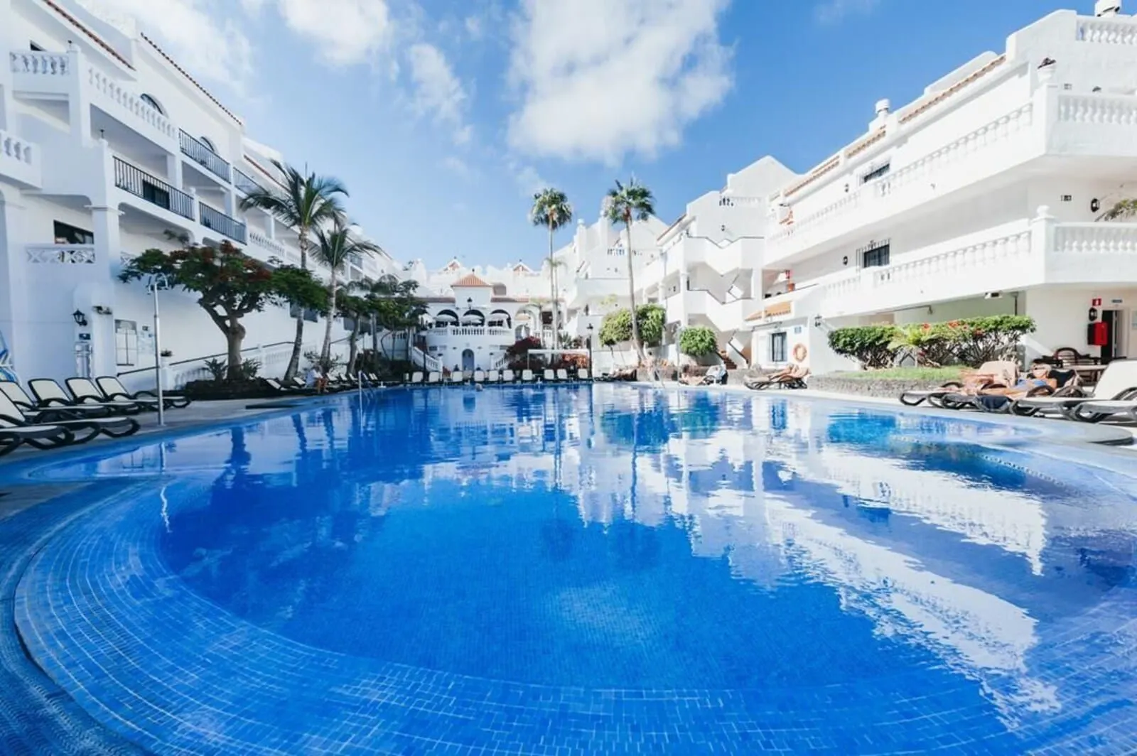 Ona Beverly Hills Heights: A pool surrounded by white buildings with balconies, palm trees, and a clear sky