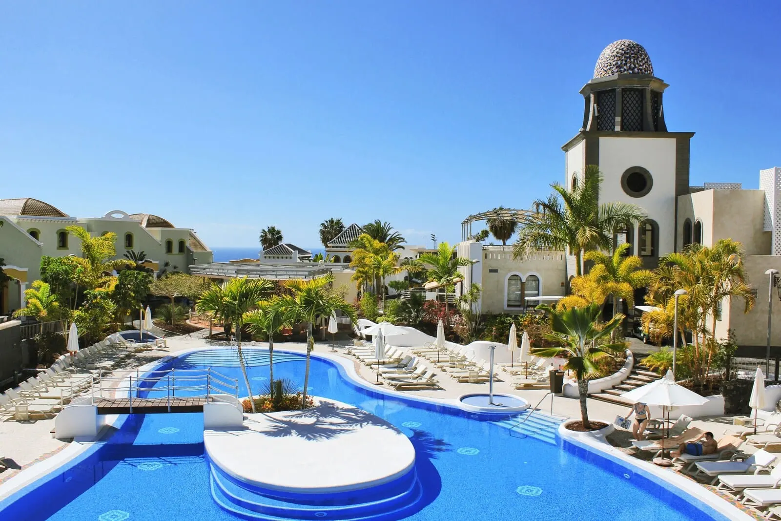 Hotel Suite Villa María: A resort pool area with lounge chairs, palm trees, and a building with a dome