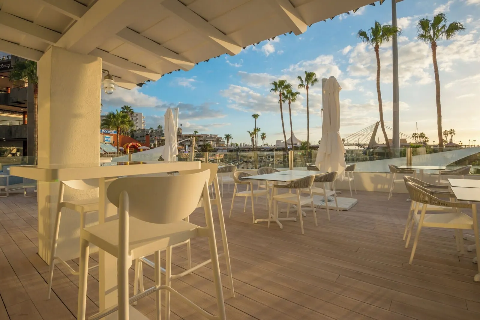 HOVIMA La Pinta Beachfront Family Hotel: An outdoor seating area with tables and chairs, palm trees, and a view of the cityscape