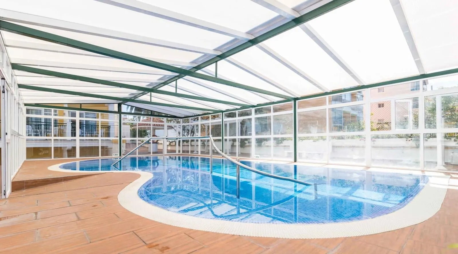 Apartamentos La Carabela: An indoor swimming pool with clear glass walls, a wooden deck, and a metal railing