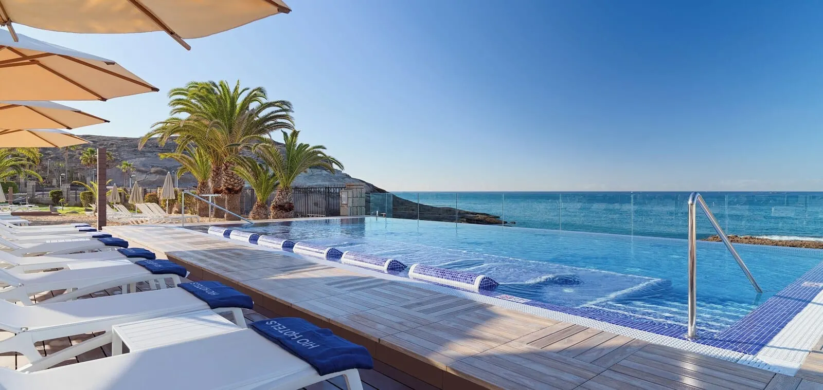 H10 Costa Adeje Palace: A poolside area with lounge chairs and umbrellas, a clear view of the ocean