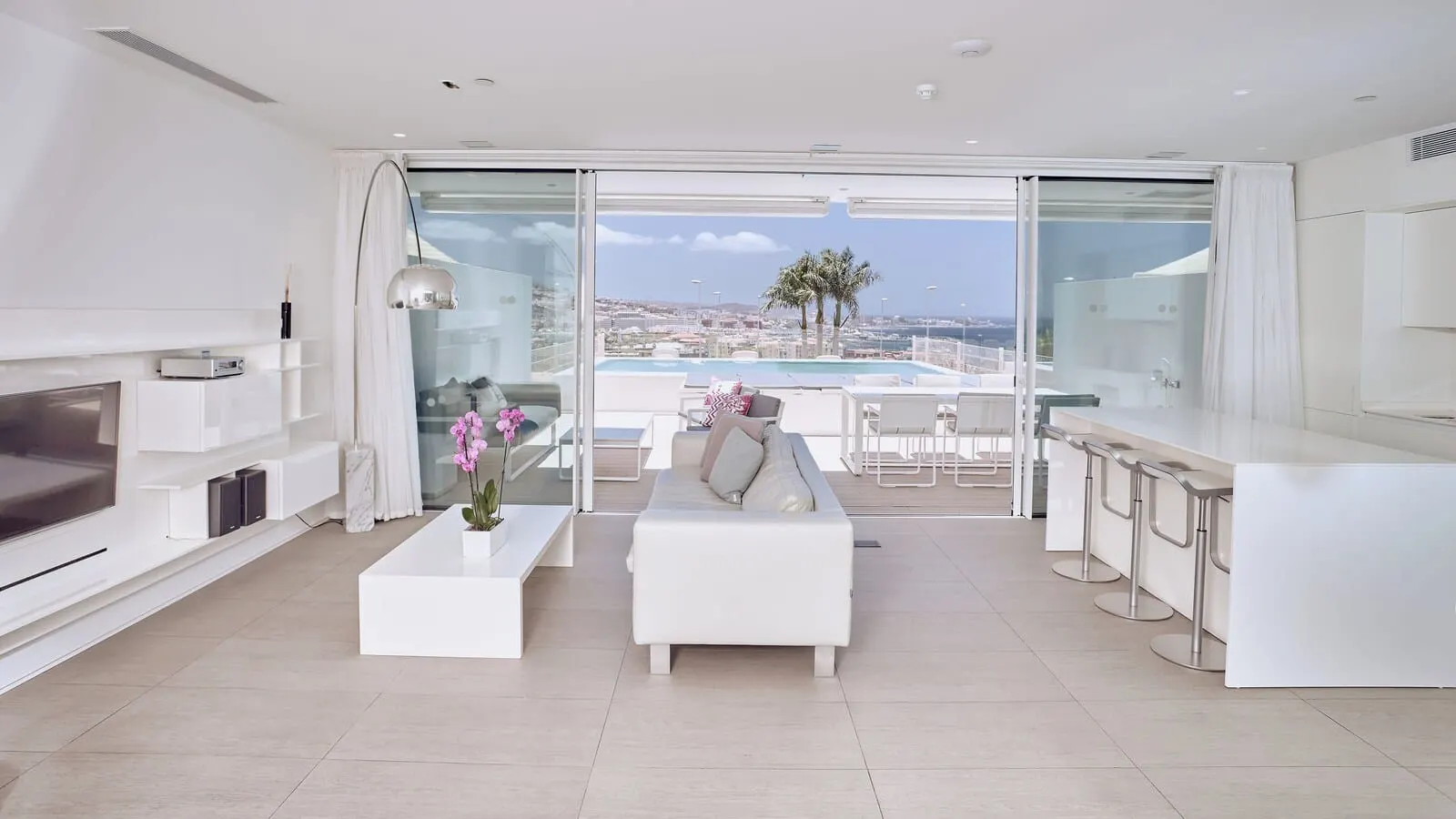 Domes Baobab Suites: A modern living room with a large TV, white furniture, a coffee table with flowers