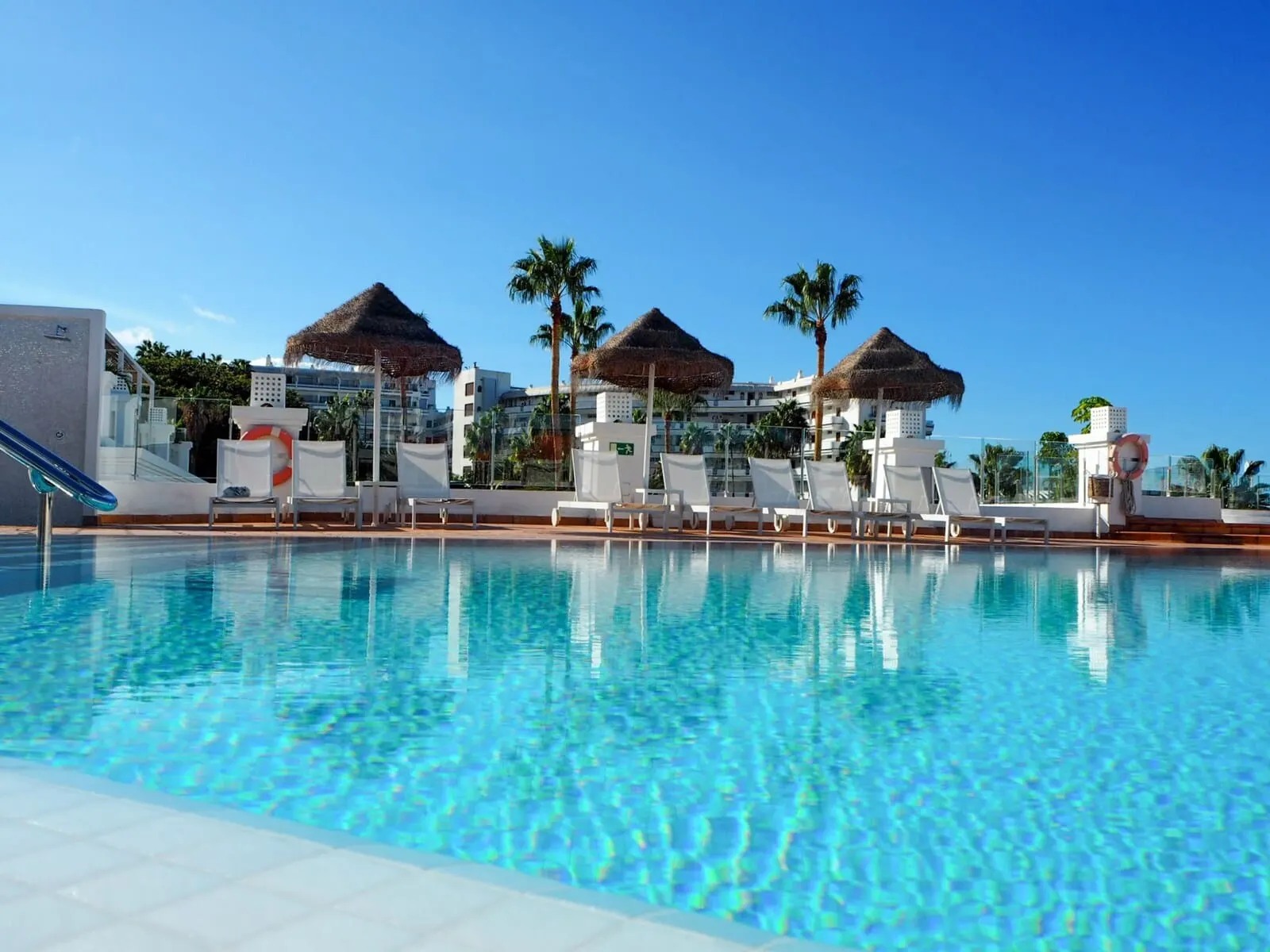 Flamingo Beach Mate: A pool area with lounge chairs and umbrellas, surrounded by palm trees and buildings