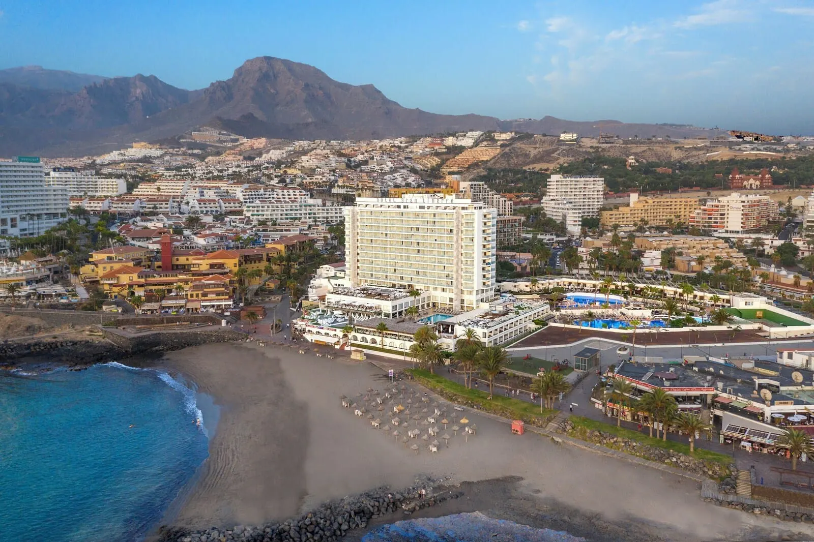 H10 Gran Tinerfe: A coastal hotel with multiple floors, a beach area with umbrellas
