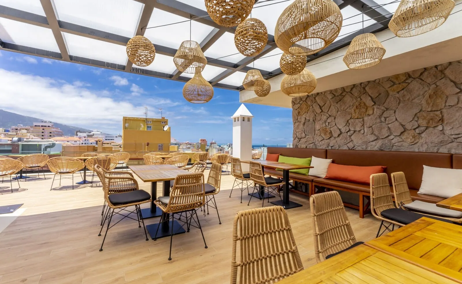 DWO Nopal: A rooftop terrace with wicker furniture, a stone wall, and a view of the city