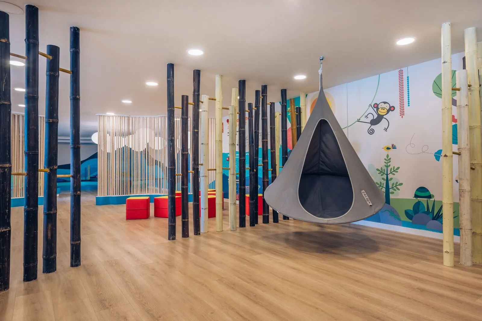 Iberostar Waves Bouganville Playa: A room with a hanging chair, bamboo columns, and a mural with a monkey