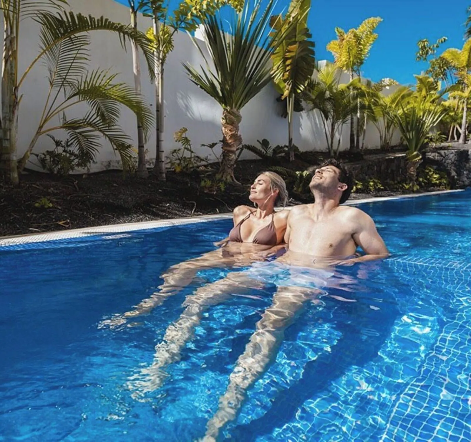 MYND Adeje: A swimming pool with clear blue water, surrounded by palm trees and a white wall