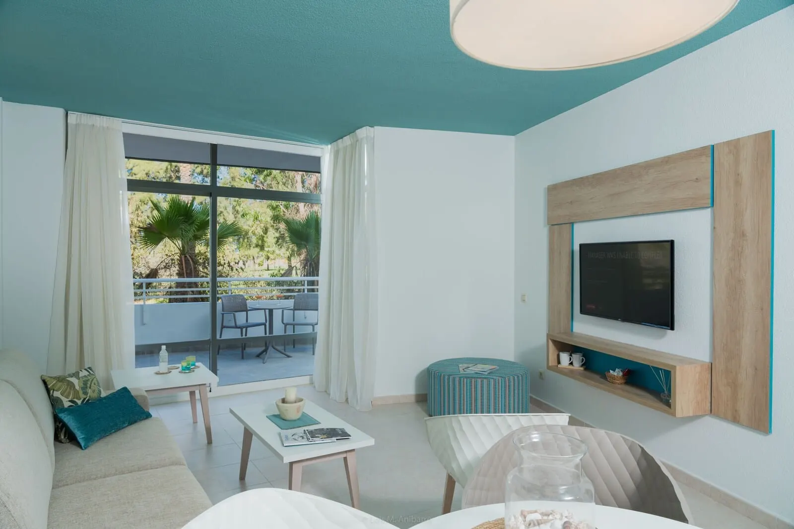 Gara Suites Golf & Spa: A modern living room with a sofa, coffee table, and ottoman, a TV mounted on the wall