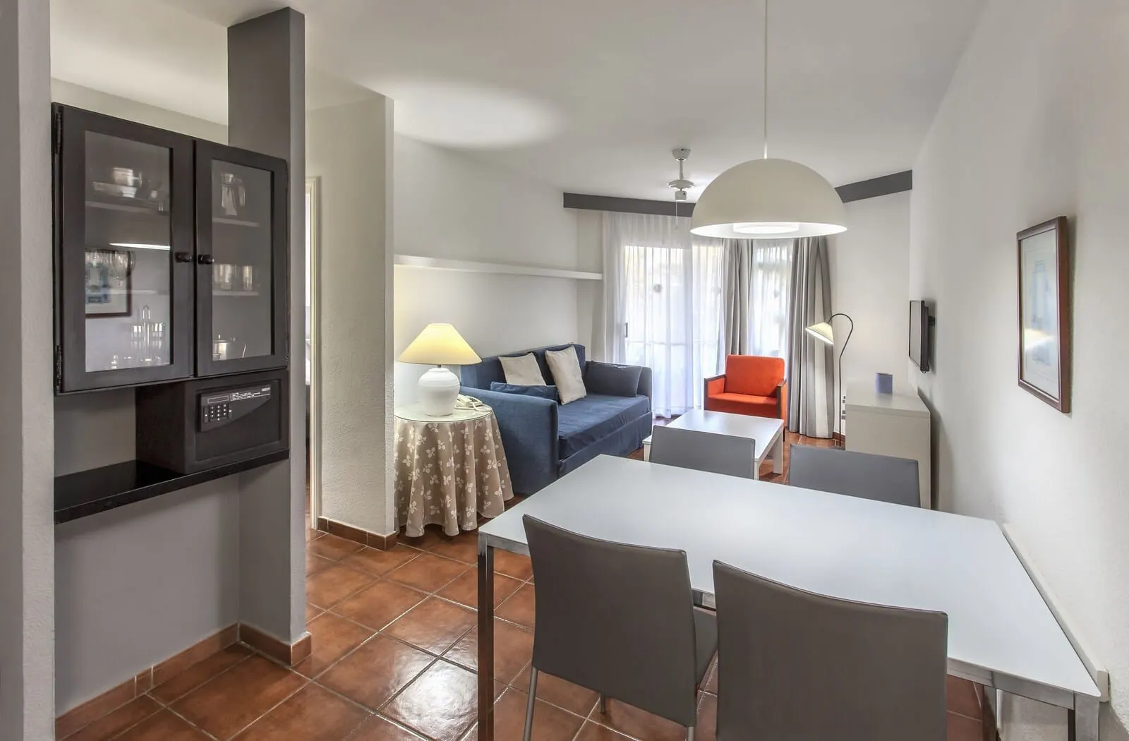 HG Tenerife Sur: A modern living room with a sofa, a dining table, and a kitchen area with cabinets