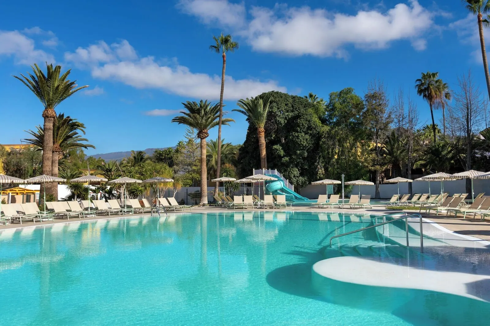 Sol Arona Tenerife: A swimming pool with a water slide, surrounded by palm trees and lounge chairs