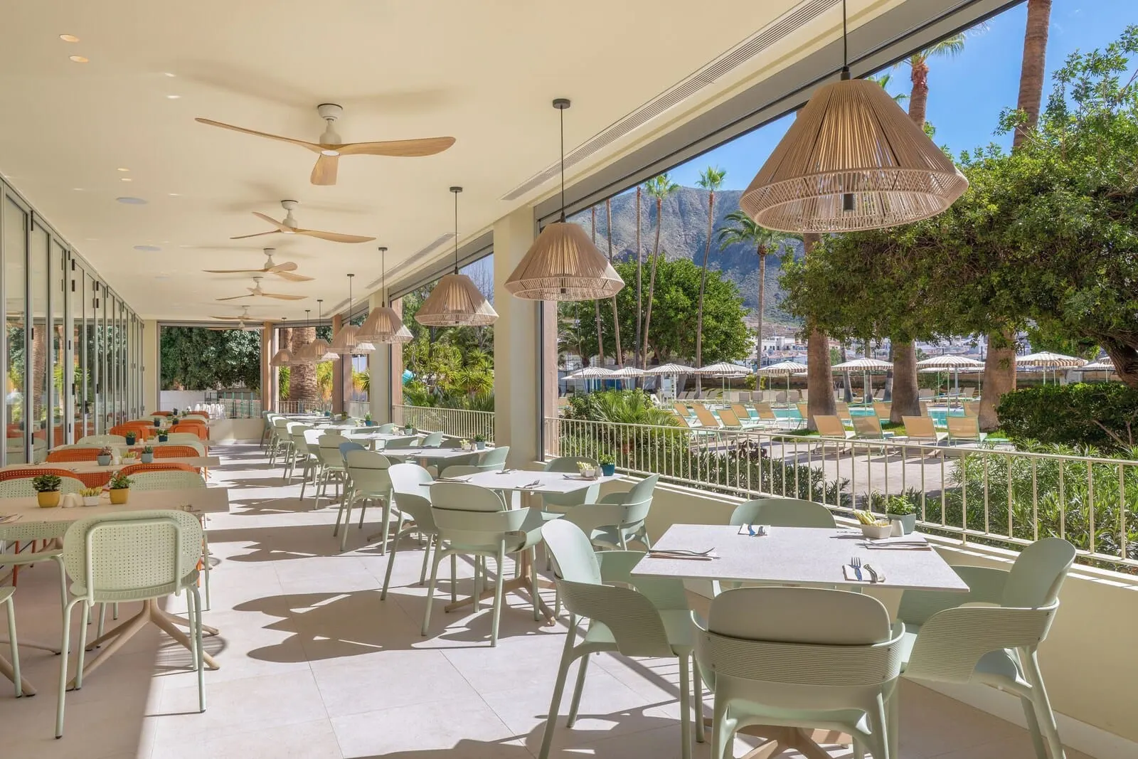 Sol Arona Tenerife: A sunlit outdoor dining area with tables and chairs, ceiling fans