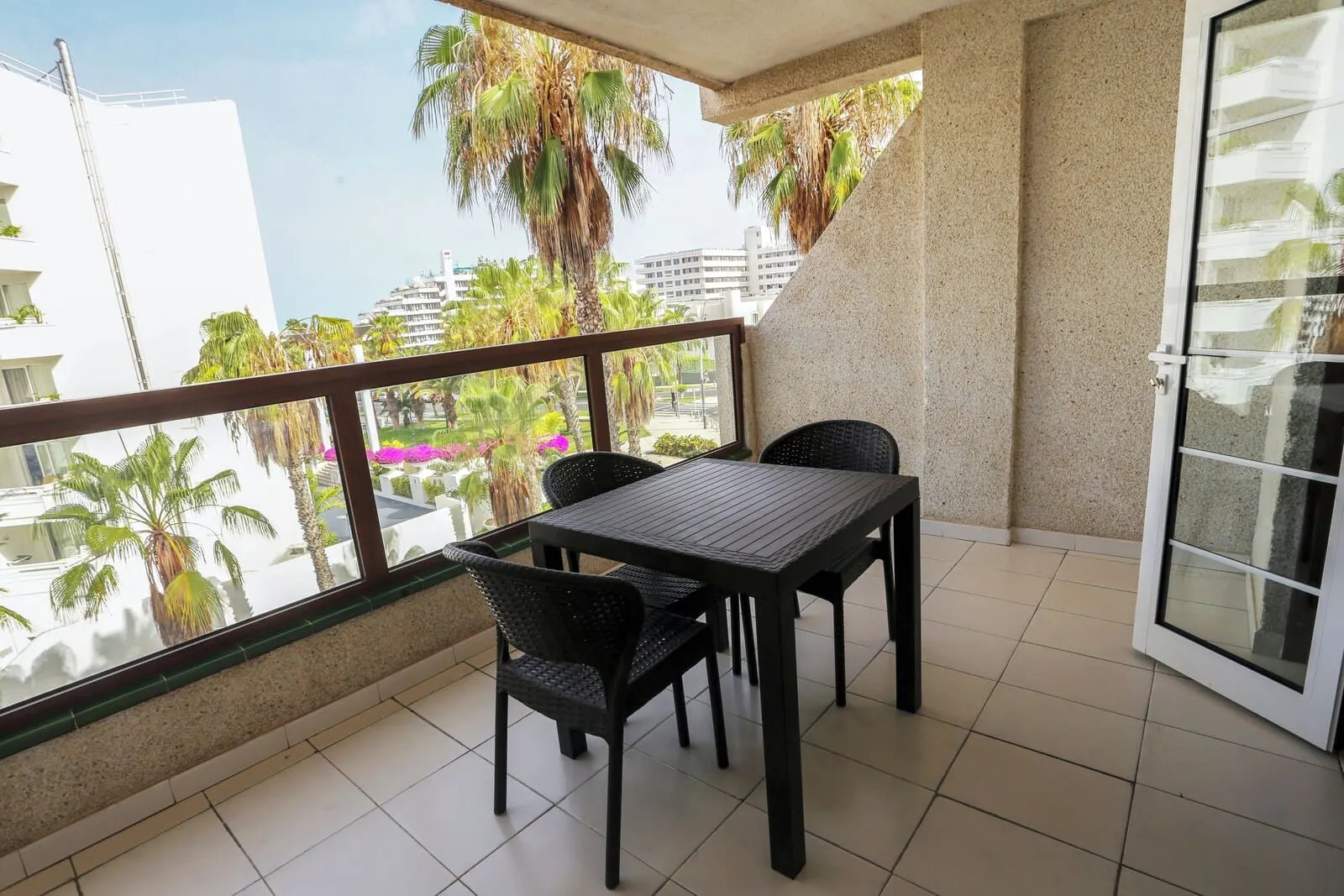 Hotel Andorra: A balcony with a table and chairs, a view of palm trees and buildings, and a glass door