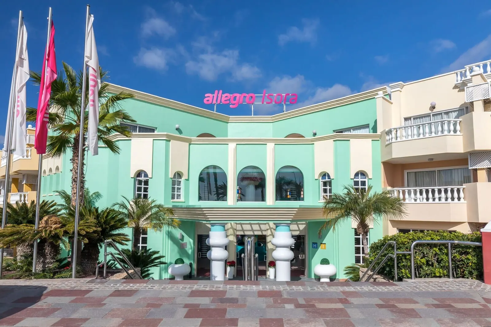 Servatur Isora Suites: A building with a teal facade, a balcony, and palm trees