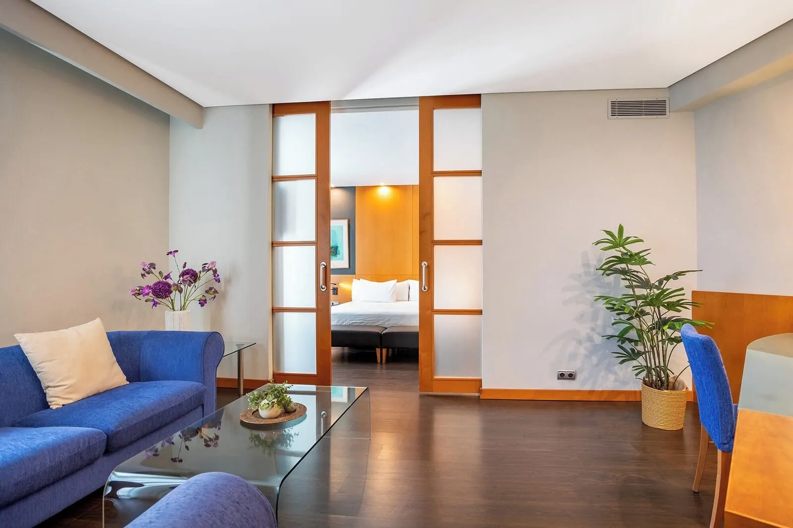 Eurostars Atlántida: A modern hotel room with a sofa, a glass coffee table, a bed, and a potted plant