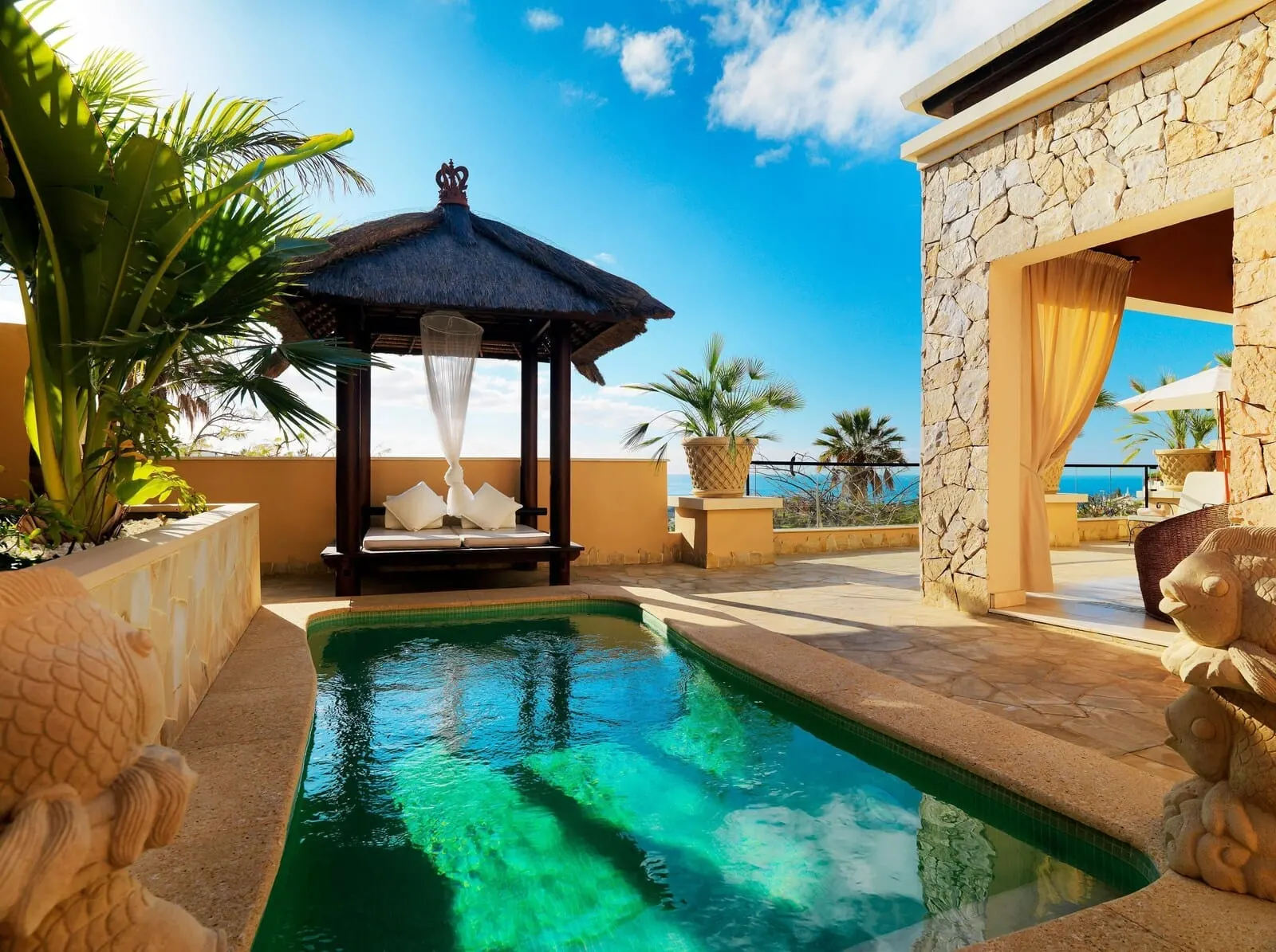 Royal Garden Villas & Spa: A pool area with a thatched gazebo, stone walls, and a view of the sea