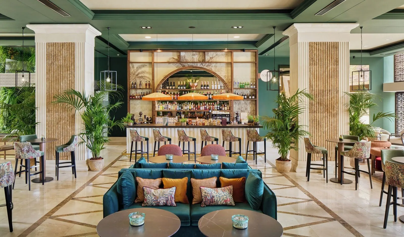 Meliá Costa Atlantis Tenerife: A bar area with a green sofa, multiple tables, and chairs, surrounded by potted plants
