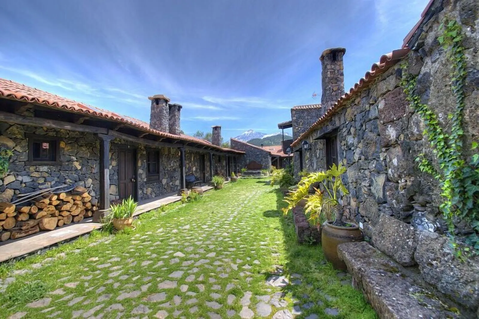Hotel Rural Caserío Los Partidos: A courtyard with stone buildings, a cobblestone path, and a mountain backdrop