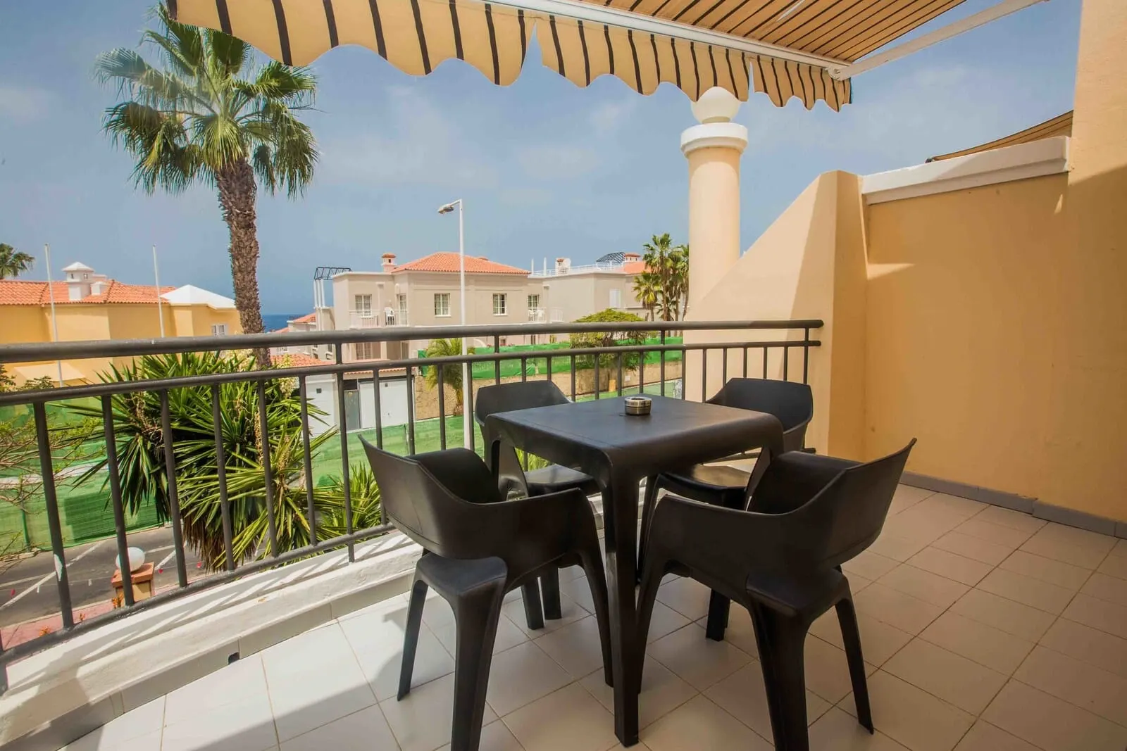 Yucca Park Aparthotel: A balcony with a table and chairs, a palm tree, and a view of buildings and a tower