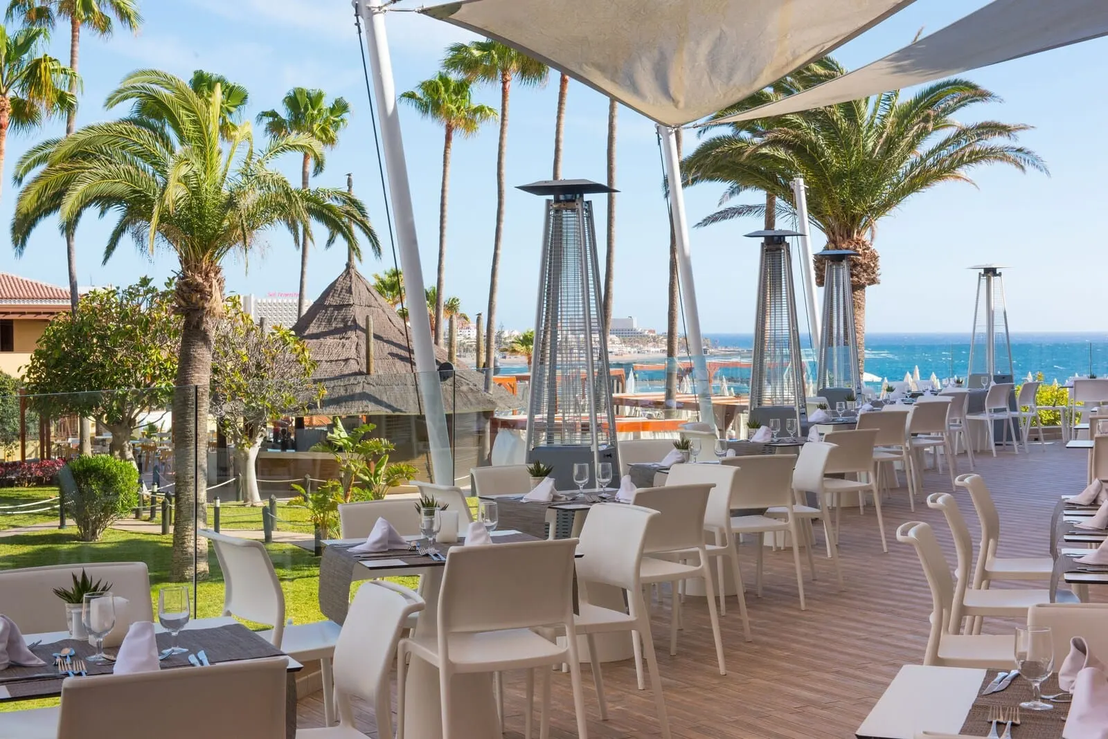 Iberostar Waves Bouganville Playa: An outdoor dining area with tables and chairs, palm trees, and a view of the ocean
