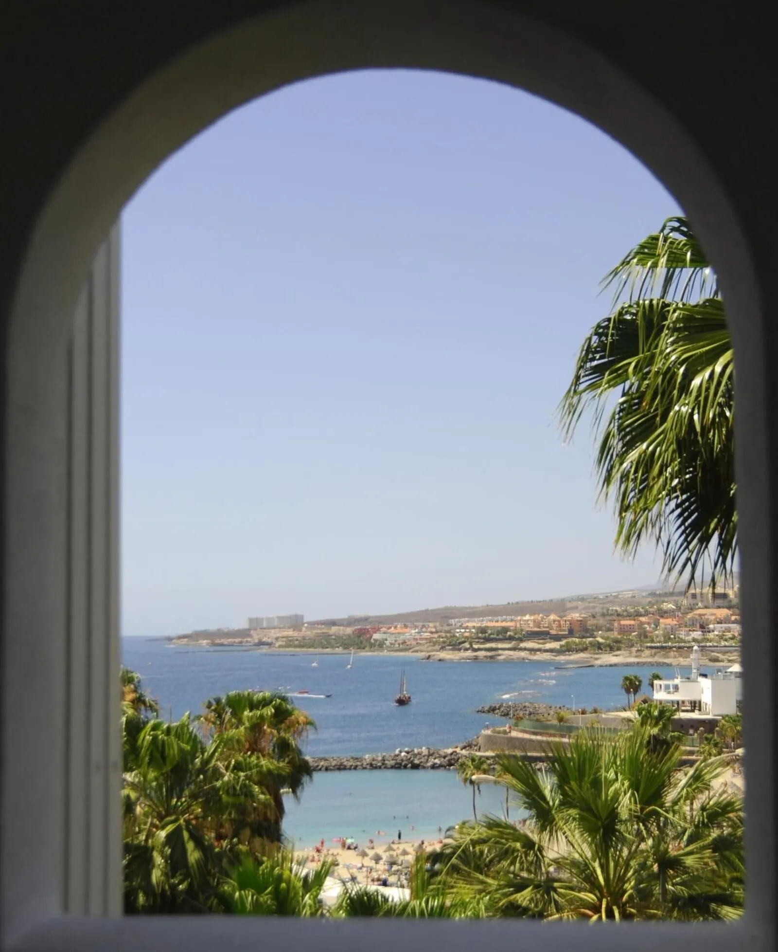 HOVIMA Atlantis: A coastal view through an arched window, featuring a beach, palm trees