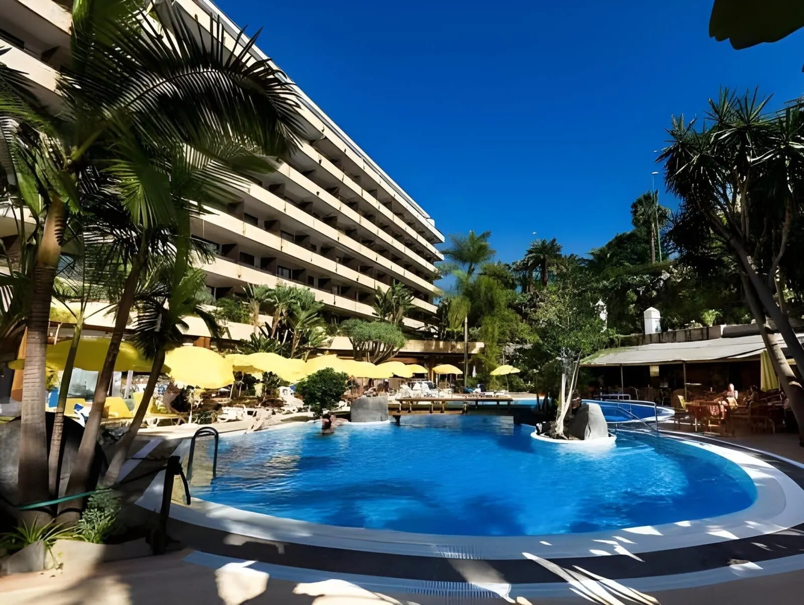 FERGUS Puerto de la Cruz: A hotel with a large pool, palm trees, and yellow umbrellas
