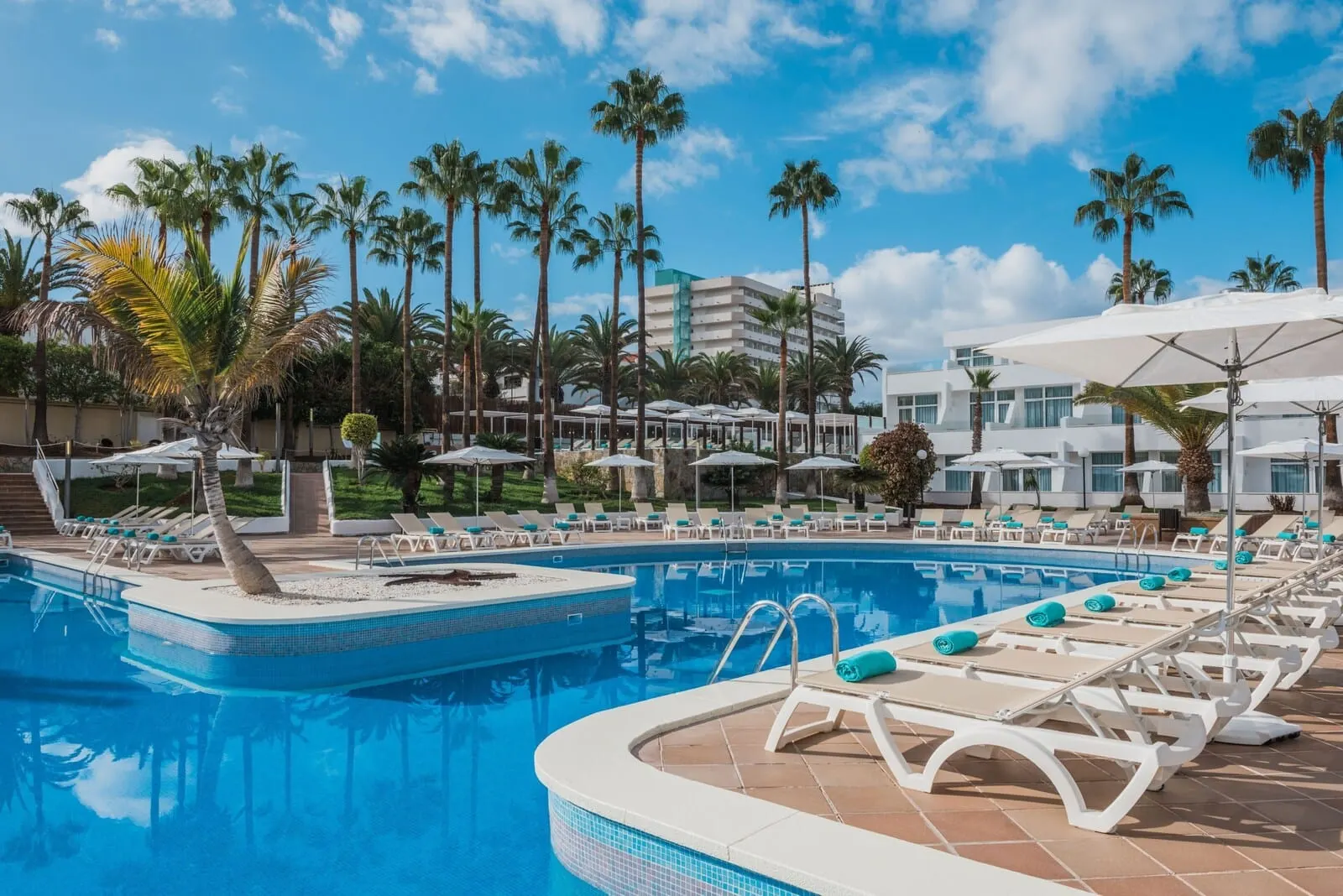 Iberostar Waves Las Dalias: A pool area with lounge chairs, palm trees, and a building in the background