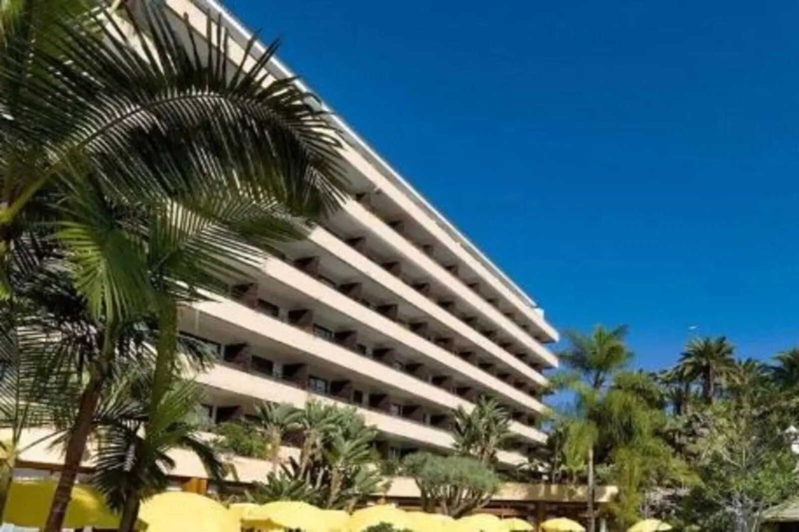 FERGUS Puerto de la Cruz: A multi-story hotel with a curved facade, surrounded by palm trees and yellow umbrellas