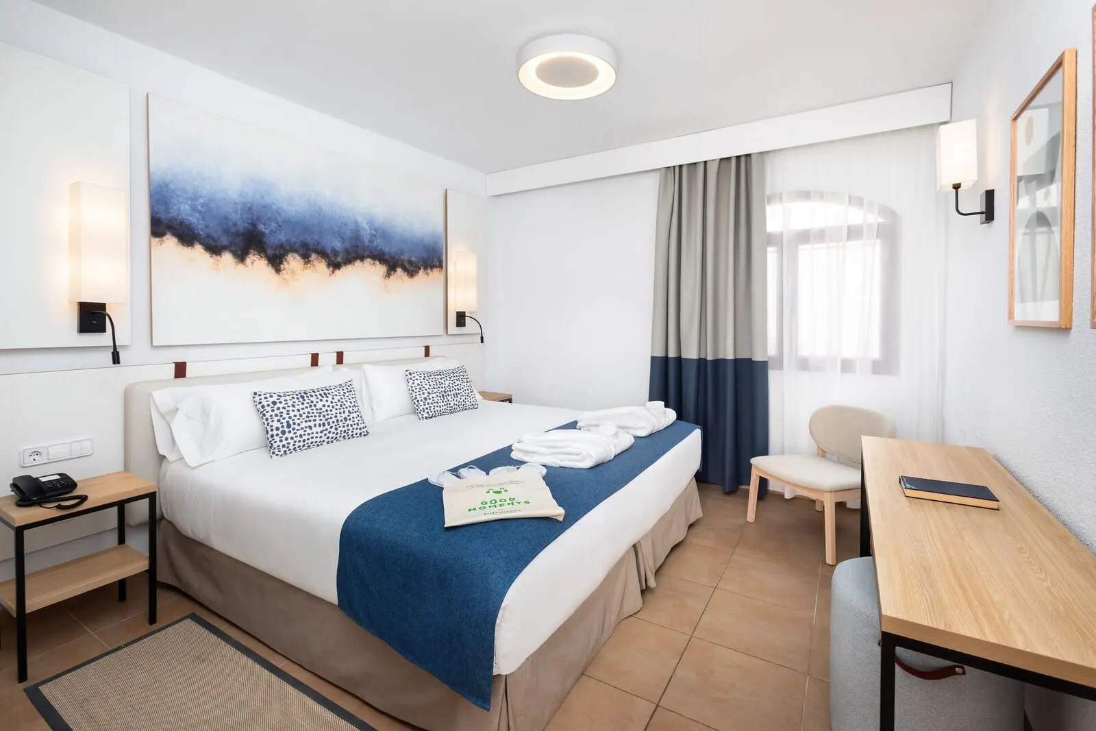 HD Parque Cristóbal Tenerife: A hotel room with a neatly made bed, a desk, a chair, and a large window with curtains