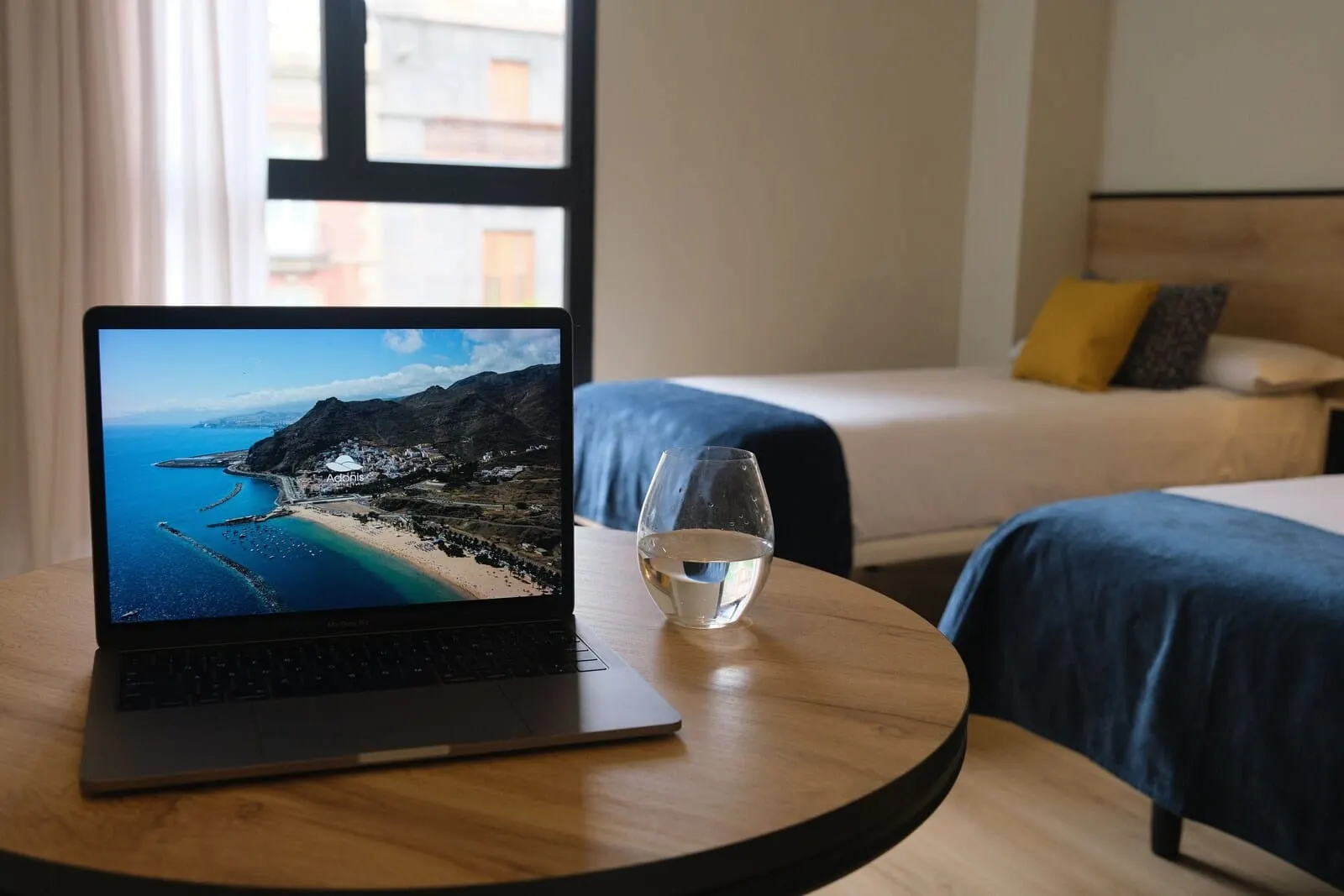 Hotel Adonis Capital: A laptop on a round table with a glass of water, a bed with blue bedding