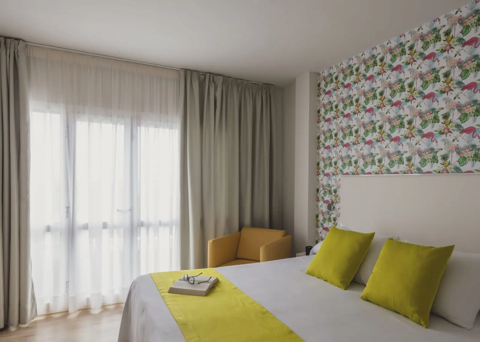 Flamingo Beach Mate: A hotel room with a large bed, a chair, and a window with sheer curtains