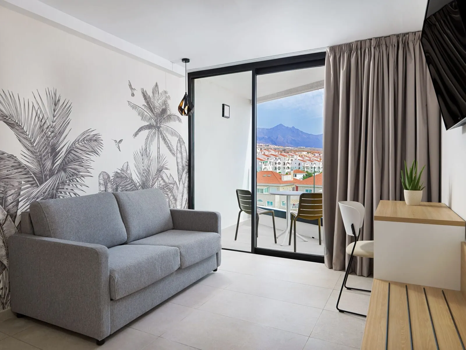 MYND Adeje: A modern living room with a grey sofa, a dining area with chairs
